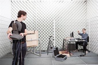 Dieses Bild zeigt zwei männliche Studierende in einem akustischen Testraum für Schallreflexionen des Fachbereichs Medien.